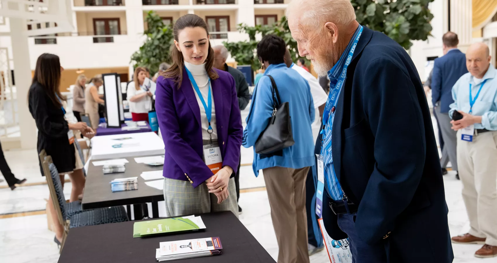 Young woman presenting educational materials to an elderly man at an event stand