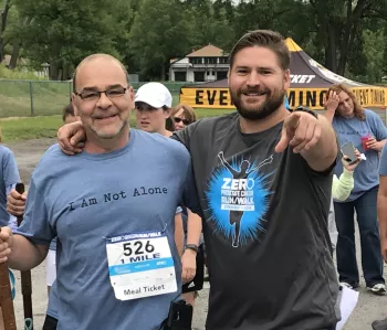Two men at a run walk event one wearing "I Am Not Alone shirt" and the other pointing at the camera