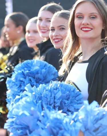 Cheerleaders lined up and holding blue pompoms