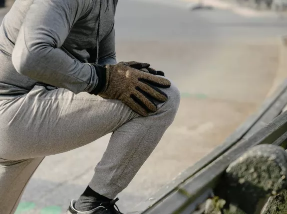 A man in cold weather jogging attire stretching on the side of the road