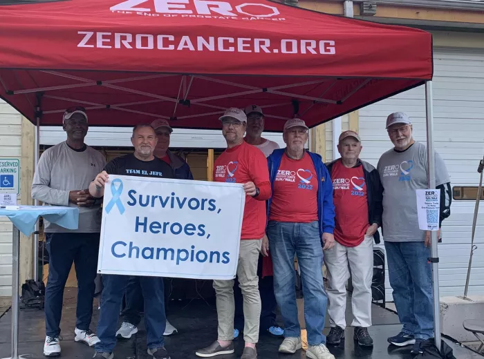 Group of men holding a sign that says Survivors, Heroes, Champions