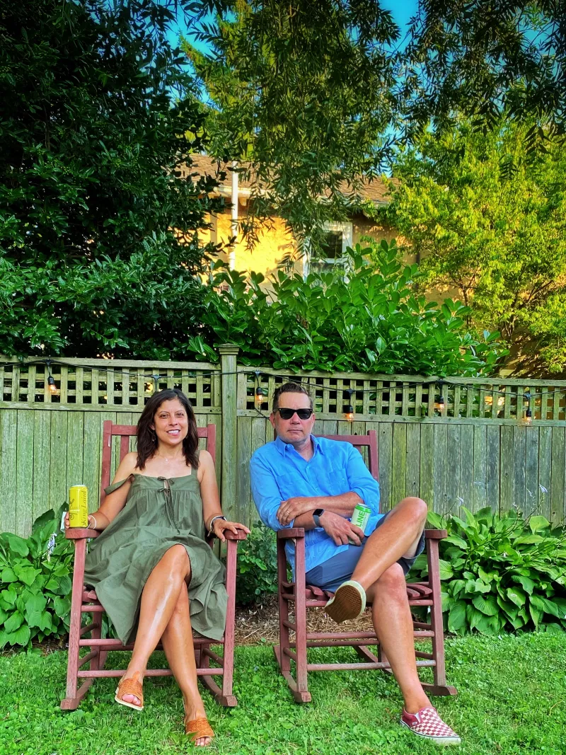 Man and woman sit on rocking chairs on green grass next to wooden fence
