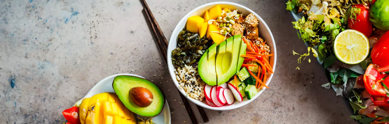 Veggie bowl with a plate of veggies next to it, as well as an avocado
