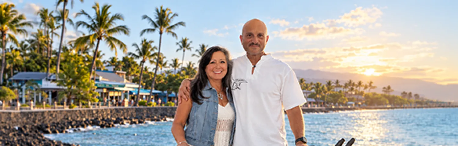 Peter Crescenti and wife standing by bike in front of water and lake and palm trees
