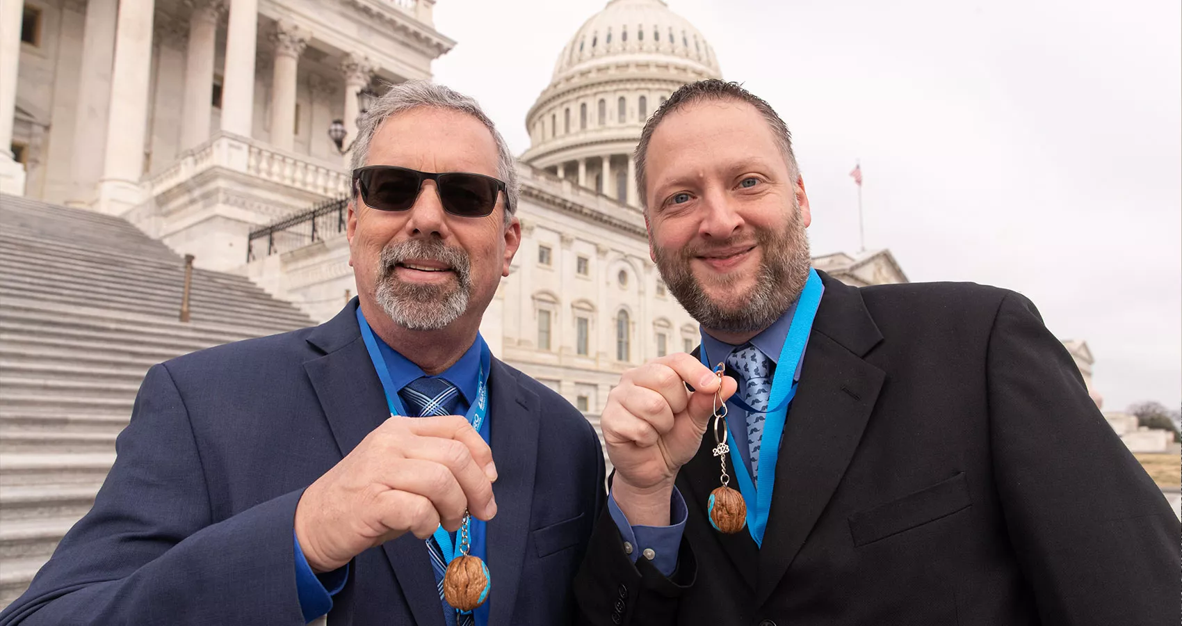 Two men in suits showing a walnut prostate cancer mascot in front of the Capitol