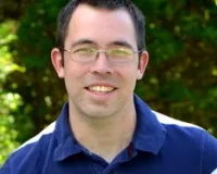 Brandon Wilhelmsen smiling at the camera in front of green trees
