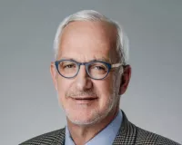 Grey-haired man with glasses wearing a suit and a tie