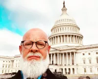 A bold man with a white beard posing in front of the Capitol