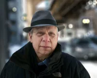 A middle-aged man with a hat and a dark coat