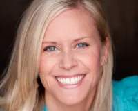 Blond Caucasian woman wearing a teal top and smiling at the camera