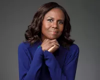 A black woman wearing a blue shirt holding her hands under her chin