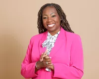 A Black woman wearing a hot pink blazer smiling and clasping her hands together