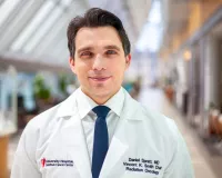 A young male doctor with brown wavy hair wearing his white coat standing in a library