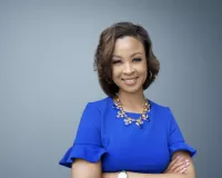 A young Black female wearing a blue blouse standing with her arms crossed