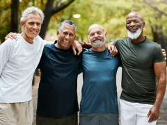 Four men standing with arms around each other shoulder to shoulder smiling