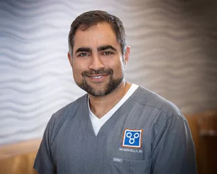 A male doctor with brown hair and a beard wearing gray scrubs