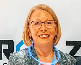 An older blonde woman with glasses standing against a ZERO sign