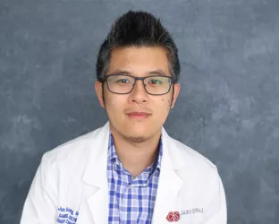 An asian doctor wearing a plaid shirt and doctors coat with glasses