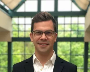A man in a suit with glasses standing in a greenhouse