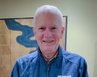 An older white man with white hair wearing a blue button-up ZERO shirt