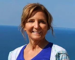 A woman standing in front of an ocean wearing a blue nike shirt and a striped sports jacket