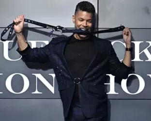 Wilson Cruz holding a belt with it in his mouth walking down the runway