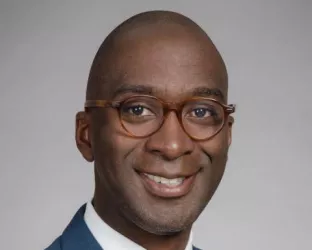 A Black man wearing a suit and glasses, posing for his headshot