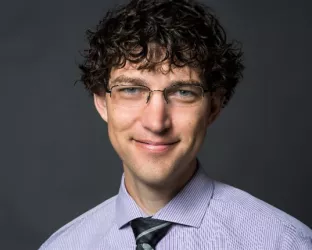 A young man with glasses and curly dark hair