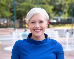 Courtney Bugler in a blue dress standing in front of water fountains