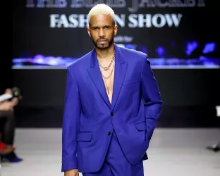 A Black man with bleach blonde hair wearing a blue suit on the runway of the Blue Jacket Fashion Show