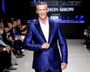 A man in his early 50s wearing a crisp blue suit and white shirt on the runway of the Blue Jacket Fashion Show