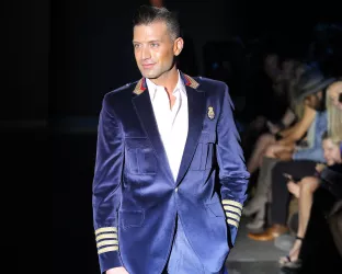 A man wearing a velvet blue and gold jacket and white shirt on a runway