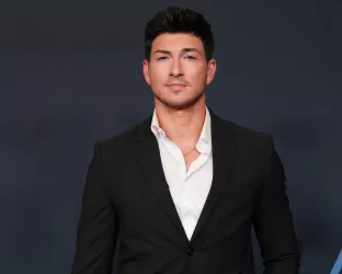 A young man with dark hair and sharp features wearing a white shirt and black suit jacket