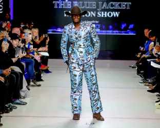 A Black man wearing a unique blue suit with a brown cowboy hat and boots