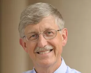 A person with short, light gray hair and glasses, wearing a light blue shirt and a red striped tie, smiling against a neutral background.