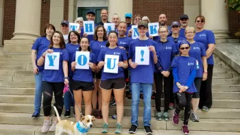 Group of people in matching shirts with cancer ribbons on them holding up signs that spell out "Thank You!" 