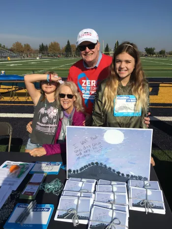 A family stands behind a table of artwork saying "I wish one day cancer would be a zodiac sign"