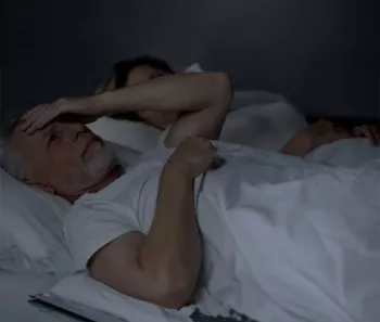 A man laying in bed looking distressed and a woman next to him