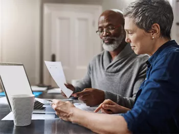A man and woman sitting at a desk looking at paperwork 