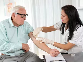 A senior man with his sleeve rolled up while a doctor performs a blood draw