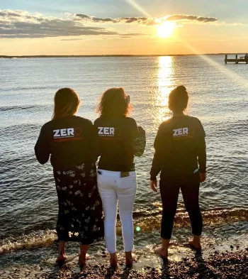 Athena Bogdanos and others looking at the sunset on the beach wearing ZERO Prostate Cancer shirts