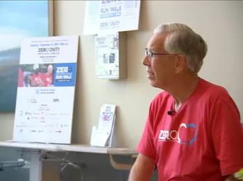 Prostate cancer survivor, Bob Lane, sitting in the waiting room wearing a red ZERO Run/Walk t-shirt, next to a table with promotional and education ZERO materials