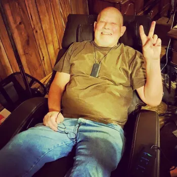 Father Brown in an EZ chair holding up a peace sign
