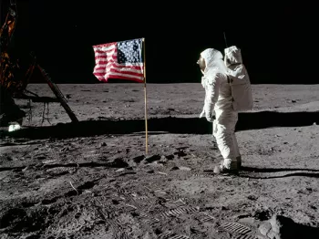 Buzz Aldrin wearing his all white space suit saluting the United States flag on the lunar surface next to the lunar rover.