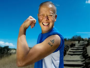 Randall (Randy) Kam smiling at the camera and flexing their well defined arms with a 26.2 running tattoo