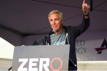 A man giving a speech at a rally with his left hand up