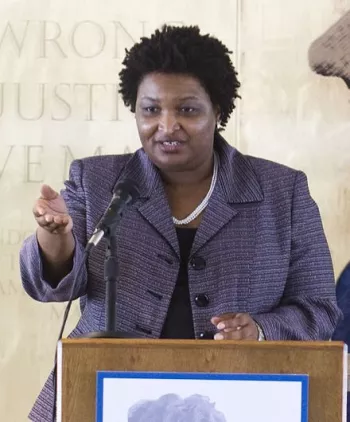 Stacey Abrams in 2012 giving a strong speech at a podium in a gray-blue blazer