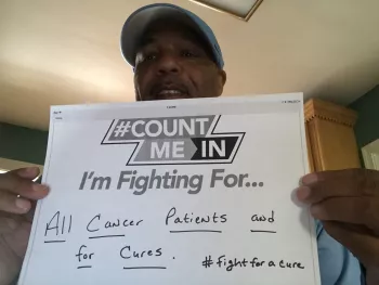 Brian Jones holding up a sign saying he is fighting for all cancer patients and a for a cure