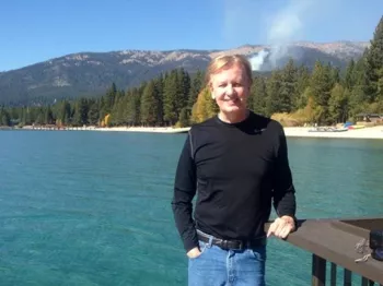 Glenn Mollette leaning on a dock by a serene mountainside and crystal clear water