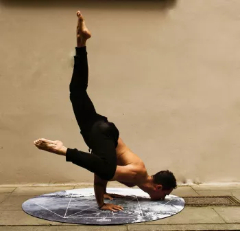 A man in black tight legging pants doing a version of Scorpion pose in yoga